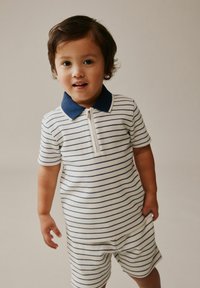 Kortærmet polo romper med striber til børn i hvid med marineblå striber, har lynlås foran og en marineblå krave. Blødt, tekstureret stof.
