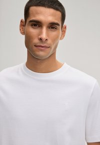 Wit katoenen T-shirt met een ronde hals, korte mouwen en een subtiel geborduurd palmbomenlogo op de linkerborst. Gladde textuur.