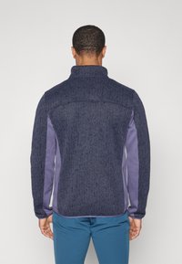 Pull en maille texturé bleu marine avec des panneaux latéraux violets et un col haut. Doté d'une coupe décontractée, avec une finition lisse sur les bords des manches.