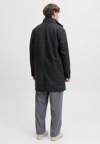 Grå uldfrakke med en tekstureret finish, høj krave og ventileret ryg. Parret med lysegrå bukser og hvide sneakers.