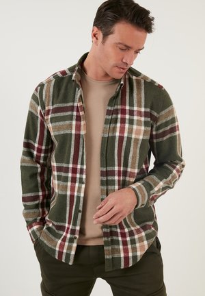 Camisa de franela a cuadros en verde, marrón y burdeos. Presenta un cierre de botones en la parte delantera, mangas largas y un cuello tipo camisa.