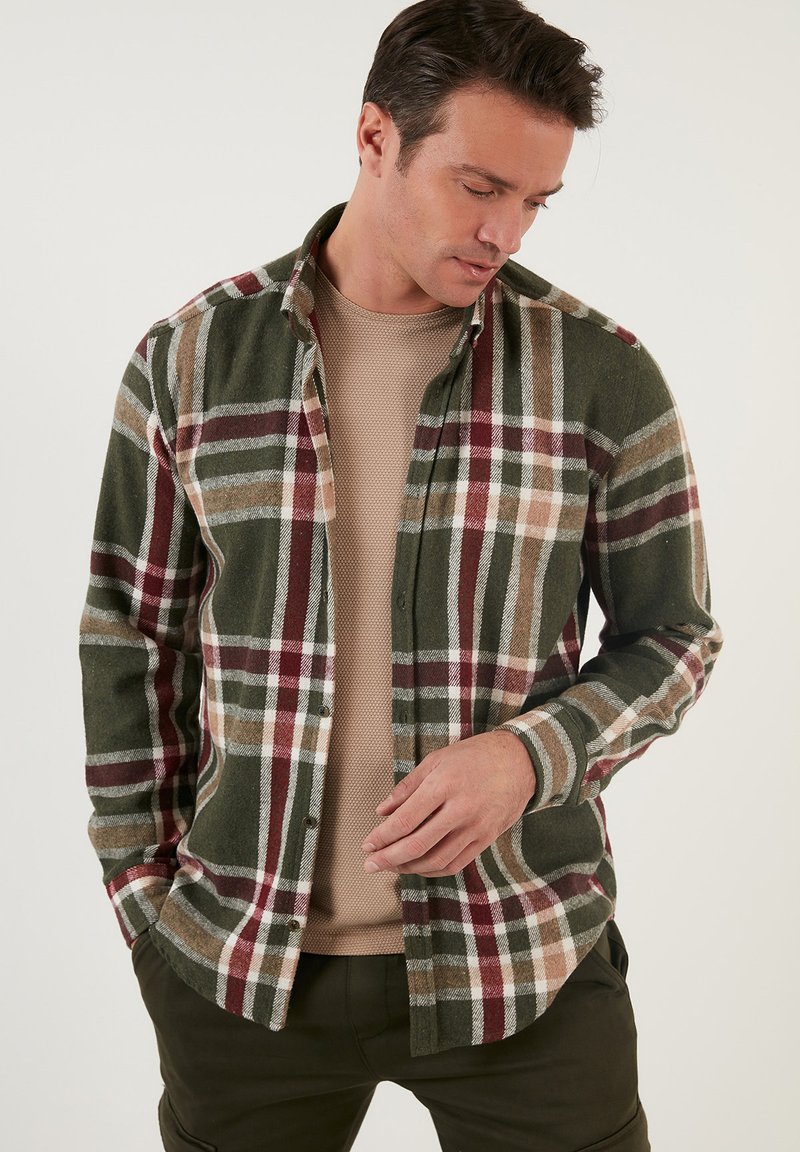 Camisa de franela a cuadros en verde, marrón y burdeos. Presenta un cierre de botones en la parte delantera, mangas largas y un cuello tipo camisa.