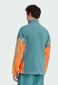 Fleece jacket with high collar. Light blue body, orange and tan sleeves. Soft texture, flexible design, and contrasting color panels.