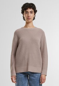 Beige teksturert strikket genser med ribbestrikket design, bred halslinje og lange ermer, kombinert med lyseblå denimjeans.