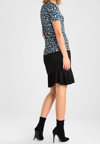 Květinový top s krátkým rukávem v tmavě modré barvě s bílými a růžovými květinami, doplněný černou sukní ke kolenům se volánkovým lemem. Černé kotníkové boty.