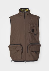Brown insulated vest with a high collar, front zip, two large zippered pockets, and a small flap pocket. Interior features a yellow pattern.