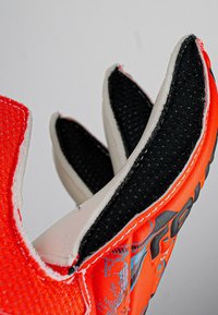 Orange Sporthandschuh mit schwarzer strukturierten Polsterung, weißen Akzenten und grafischen Elementen. Verfügt über ein eng anliegendes Design mit flexiblen Fingern.