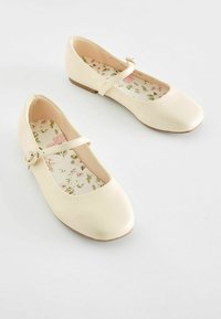 Ballerine beige con punta rotonda, dotate di una fascia con un bottone decorativo e una soletta a fantasia floreale. Materiale morbido, tacco basso.