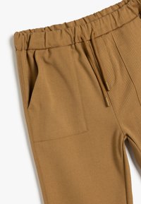 Pantalons de jogging marron avec une taille élastique, un cordon de serrage et des poches latérales ; fabriqués à partir d'un matériau texturé et durable.
