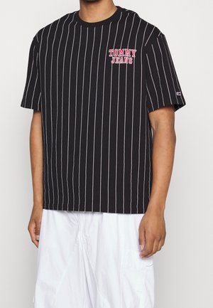 Czarny t-shirt w paski z białymi pionowymi liniami. Posiada okrągły dekolt, krótkie rękawy oraz czerwone logo "TOMMY JEANS" na piersi.