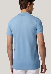 Jasnoniebieska koszulka polo wykonana z miękkiej bawełny, z klasycznym kołnierzykiem i krótkimi rękawami. Posiada logo na plecach i boczne rozcięcia u dołu.