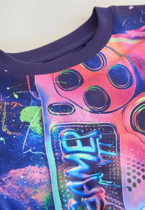 Sweatshirt coloré avec un graphique vibrant d'une manette de jeu. Le matériau est doux avec un col côtelé marine. Les accents incluent des éclaboussures de couleurs néon.