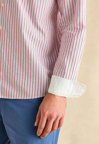 Prúžkovaná košeľa s červenými a modrými vertikálnymi pruhmi, biele golier a manžety, bavlnený materiál, zapínanie na gombíky, štíhly strih.