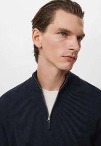 Pulover din tricot fin, de culoare bleumarin, cu guler cu fermoar, având un strat interior alb contrastant. Textură netedă și croială ajustată.