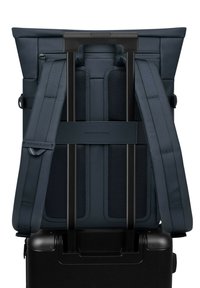 Sac à dos bleu marine avec des bretelles rembourrées, des détails en mesh et une planche pour se fixer à la poignée d'une valise. Matériau durable, lignes épurées.