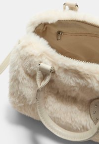 Borsa a tracolla in pelliccia artificiale color crema con manici in pelle liscia, chiusura con zip e rivestimento interno morbido. Presenta una tasca con zip all'interno.
