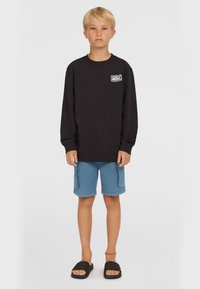 Sudadera negra de manga larga y cuello redondo, combinada con pantalones cortos azules y sandalias de tipo slide negras. Presenta un detalle de logo en la parte frontal.