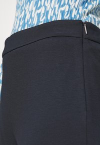 Närbild av midjan på marinblå byxor med siddragkedja bredvid en överdel med blå och vit mönstring.