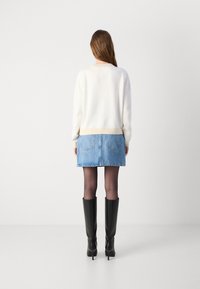 Hvit genser med beige kant, kombinert med et lyseblått denimskjørt. Svarte knelang støvler med hæl fullfører antrekket, sett bakfra.