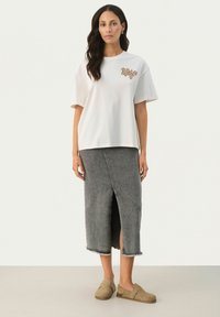 Camiseta blanca de gran tamaño con bordados florales marrones, combinada con una falda de mezclilla gris hasta la rodilla que presenta una abertura frontal y un dobladillo deshilachado. Calzado casual.