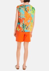 Bunte Bluse mit einem tropischen Blattmuster in Grün, Orange und Blau; kombiniert mit orangefarbenen Leinen-Shorts. Lässiger Baumwollmischstoff.