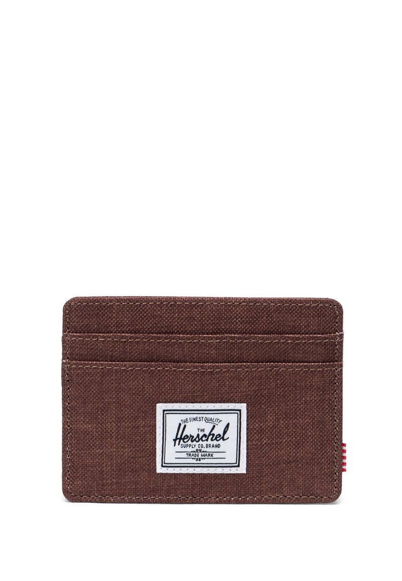 Ruskea kankainen korttikotelo, jossa on neljä korttipaikkaa, valkoinen logotägi ja punaraidallinen kangastagi sivulla. Rosoista pintaa, minimalistinen muotoilu.