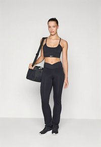 Črn športni kratki top združen s črnimi pajkicami z visokim pasom. Črna športna torba leži na levem ramenu, športni črni čevlji pa dopolnjujejo videz.