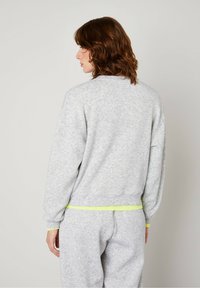 Gray jersey sweatshirt with relaxed fit, featuring ribbed cuffs and hem, accented with bright yellow trim at the waist and cuffs.