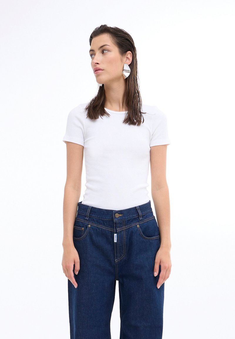 Tricou alb cu mânecă scurtă, ajustat, asortat cu blugi dark blue cu talie înaltă, având două buzunare frontale și cusături vizibile.