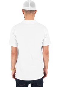 Witte korte mouwen t-shirt met een gebogen zoom en geen zichtbare graphics, gedragen met blauwe jeans. Mesh-achterkant witte pet zichtbaar.