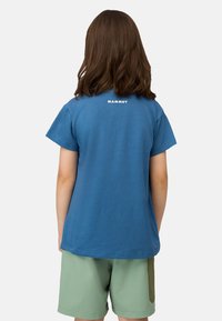 Blauwe katoenen t-shirt met korte mouwen, voorzien van een wit "MAMMUT" logo op de achterkant. De onderrand is recht en de stof lijkt glad.