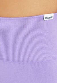 Fascia viola a coste dell'abbigliamento sportivo con un leggero lucido, dotata di un piccolo etichetta bianca con la scritta "SMILODOX." Texture liscia su tutta la superficie.