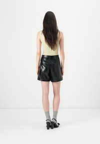 Svarte skinnshorts med rullekanter, glatt tekstur, kombinert med en lysegrønn utenermet topp og grå knelange sokker.