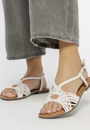 Sandalias trenzadas de cuero blanco con suela plana y tira en el tobillo. Presentan un diseño de punta abierta, correas texturizadas y una plantilla de color natural.