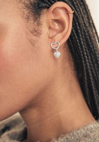 Pendientes plateados en forma de corazón con un colgante texturizado en forma de corazón, que muestran un acabado metálico suave y un brillo sutil.