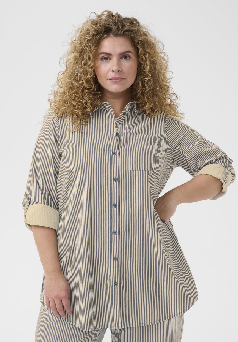 Blouse rayée avec un devant à boutons, un col, des manches retroussées avec des poignets contrastés, et une coupe loose.