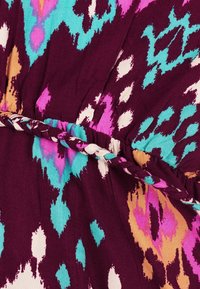 Ceinture en tissu tressé sur une robe avec un motif abstrait coloré en violet, bleu sarcelle, rose, blanc et orange.