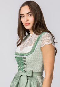Green patterned dress with a lace white blouse, featuring a corset-style front, decorative ribbon accents, and a bow at the waist.