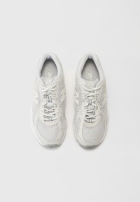 White athletic sneakers featuring a mesh upper, laced design, padded collar, and logo accents on the sides and tongue.