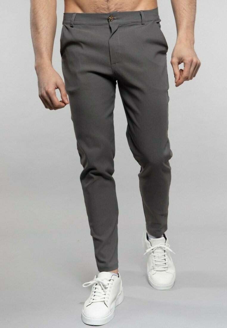 Pantalons gris slim-fit en tissu lisse, avec une fermeture éclair et un bouton à l'avant, associés à des baskets blanches.