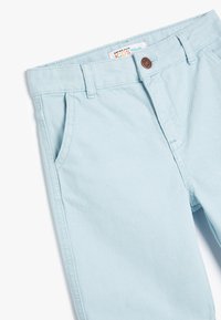 Lyseblå denim jeans til børn med klassisk fem-lomme design, bæltestropper og en rund brun knap i taljen.