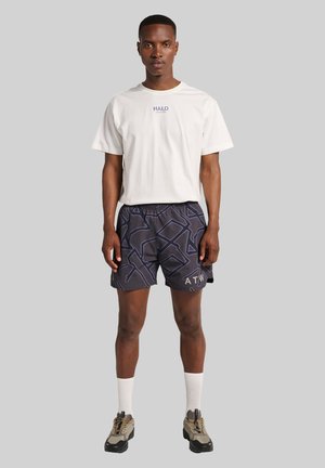 Hvidt bomulds T-shirt med "HALO" logo, parret med sorte shorts med et geometrisk mønster og "ATN" tekst, suppleret med hvide sokker og multicolor sko.