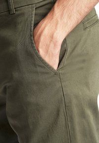 Olijfgroene broek gemaakt van zachte stof, met een voorzak met een gladde textuur en scherpe naaddetails.