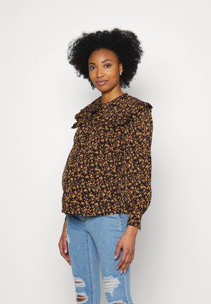 Blusa preta floral com colarinho pregueado, apresentando pequenas flores amarelas e vermelhas. Usada sobre jeans rasgados de cor azul clara, com mangas longas.