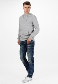 Hoodie gris avec une poche avant, col à cordon de serrage ; associé à un jean bleu foncé et des baskets blanches avec des accents rouges. Design simple, coupe décontractée.
