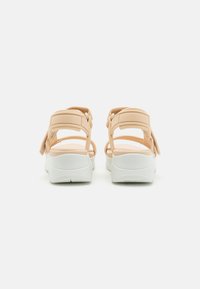 Sandali color pesca con più cinturini, dotati di una suola bianca e imbottita e una texture liscia. Chiusura con velcro per una vestibilità regolabile.