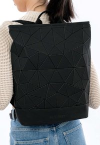 Juodas kuprinės su geometriniu raštu, pagamintas iš tekstūruotos medžiagos su trikampiais dizainais. Turi reguliuojamas petnešas ir tvirtą pagrindą.