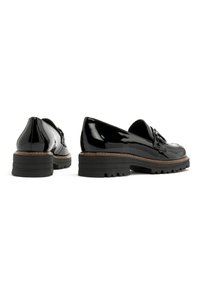 Zwarte lakleren schoenen met een ronde neus, decoratieve hardware en een chunky zwarte rubberen zool met groefpatronen.