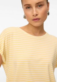 Geel en wit gestreepte shirt met een relaxte pasvorm, voorzien van een ronde halslijn en een zachte textuur, gecombineerd met grote zilveren ronde oorbellen.