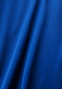 Tissu bleu lisse avec des plis doux créant des ombres et des reflets délicats sur la surface.